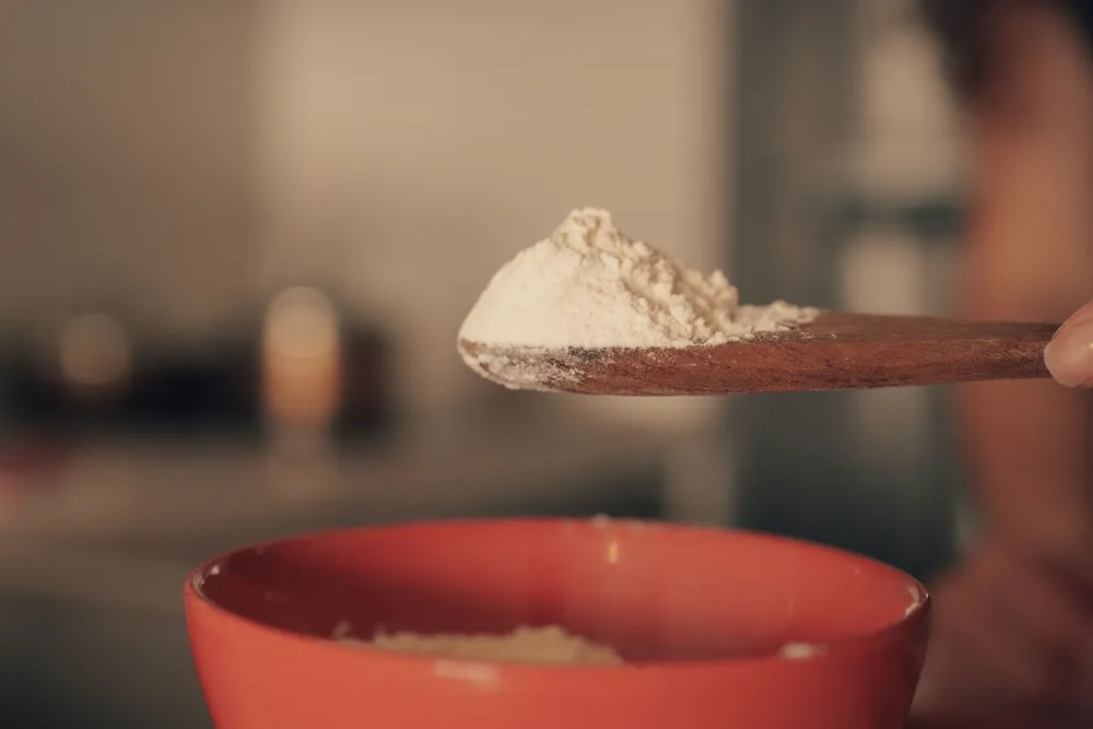 A wooden spoon of fine powder held above a red mixing bowl