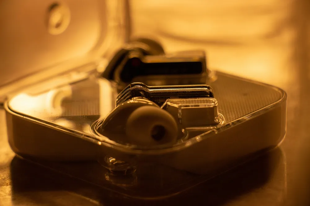 Earbud-style hearing devices resting in an open charging case in warm evening light