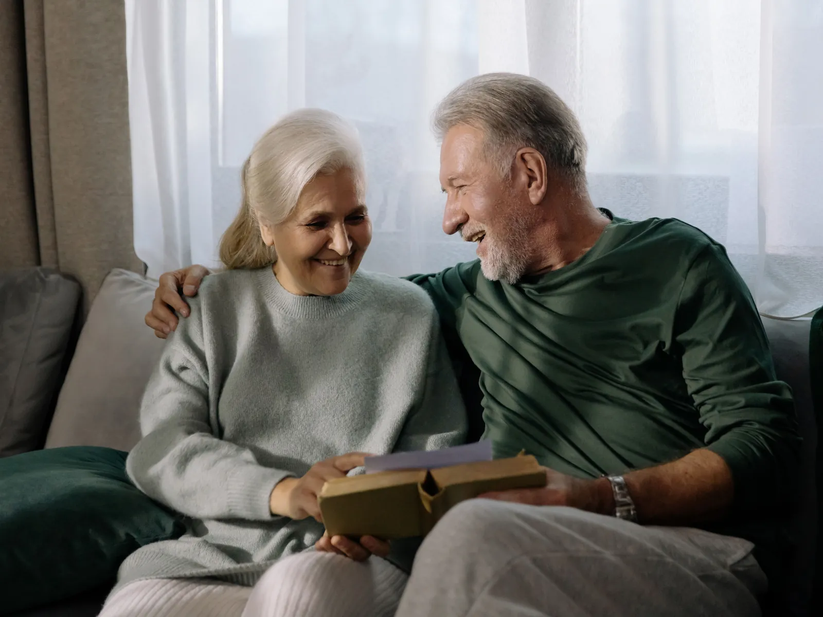 An older couple sitting together on a sofa, talking and laughing