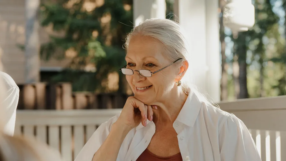 A woman in her seventies listening, resting her chin on her hand on a sunlit porch