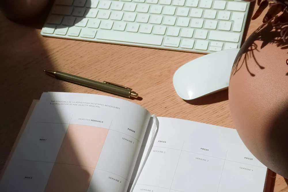 An open weekly planner with a pen and keyboard on a sunlit desk
