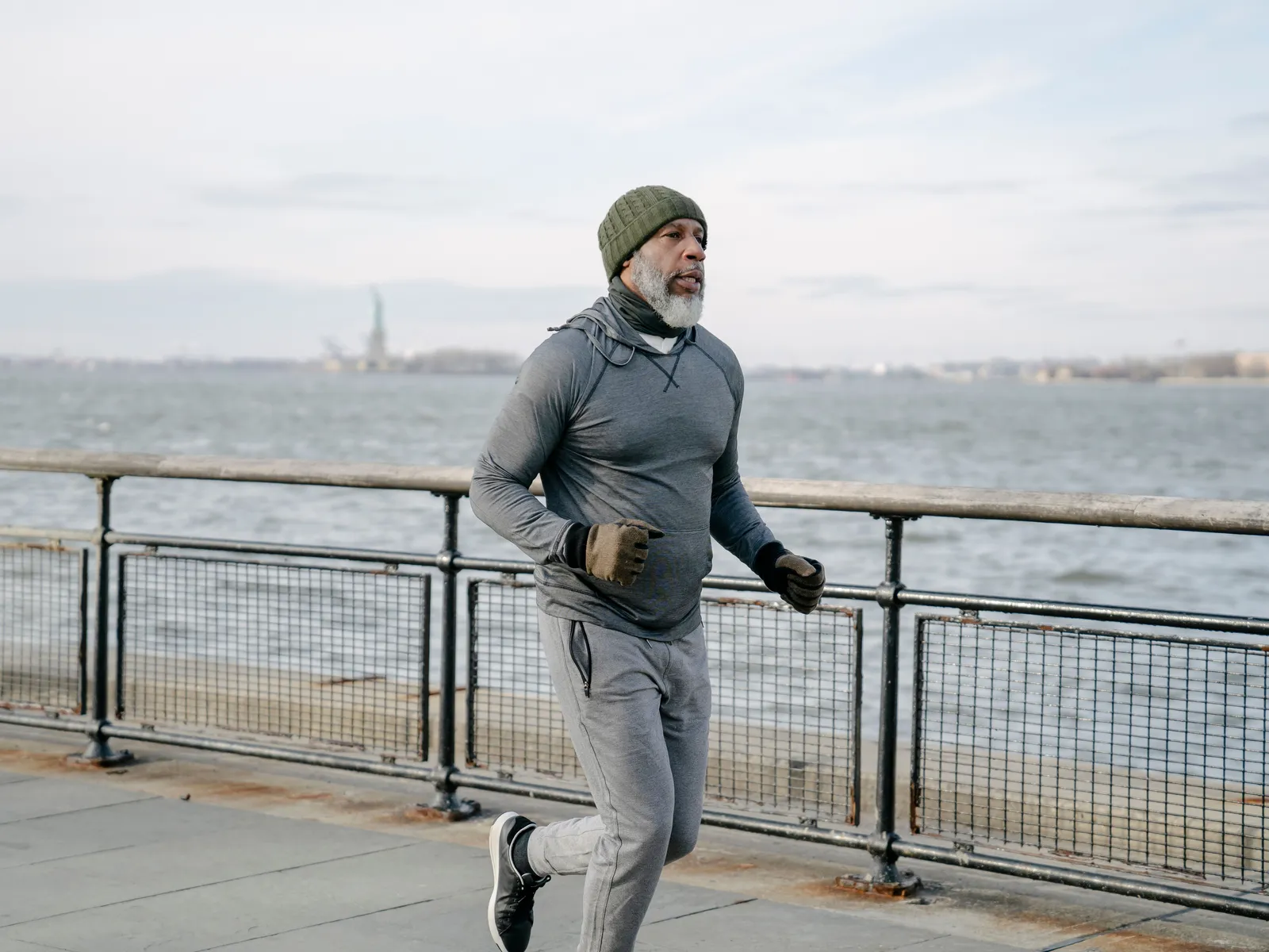 A man in his sixties jogging along a waterfront path in a knit cap and gloves