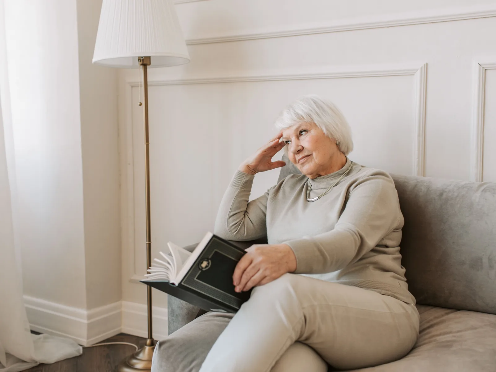 A woman in her sixties reading a book beside a bright window