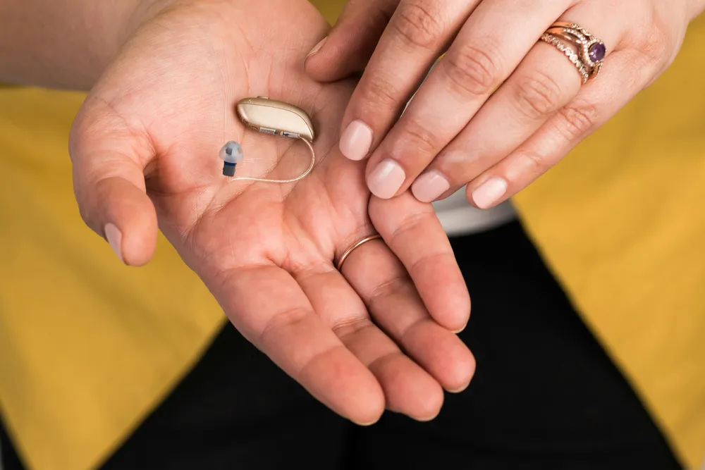 A small hearing aid resting in a woman's open palm