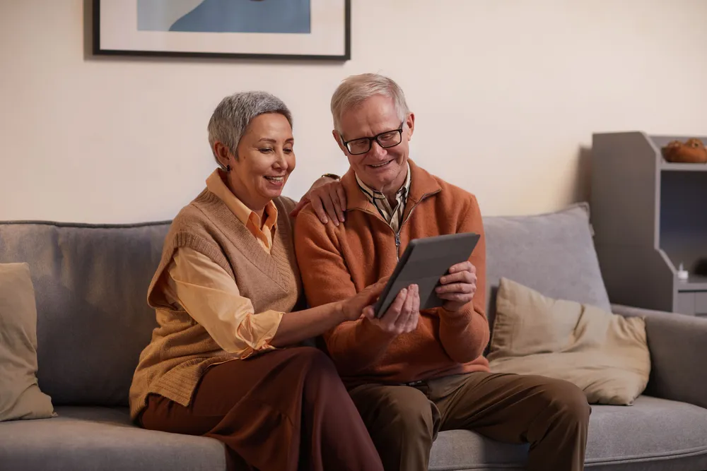 An older couple on a sofa, smiling as they browse on a tablet together